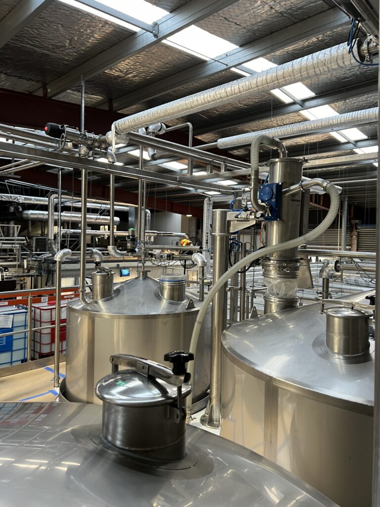 Large stainless steel tanks and hanningfield pipelines inside an industrial facility.