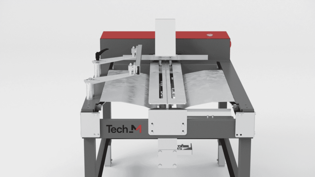 A metal machine labeled Tech-M automatically bends a sheet of metal, demonstrating a sheet metal folding or forming process on a gray and red industrial worktable.