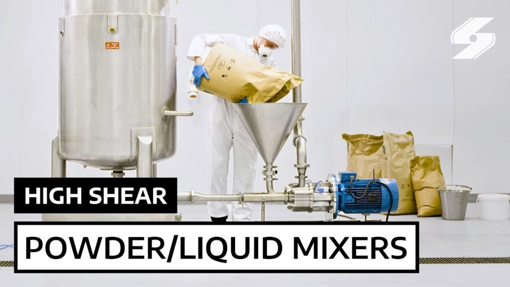 A person wearing protective gear pours powder into a stainless steel industrial mixer labeled High Shear Powder/Liquid Mixers, designed for lowering energy consumption, in a clean white facility with sacks and equipment in the background.